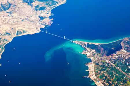 Aerial view of Osmangazi Koprusu steel suspension bridge across Gulf of Izmit, near cities Gebze, Hersek. Many tiny ships in blue sea water, port, dock, long winding road, colorful land plots. Turkeyの写真素材