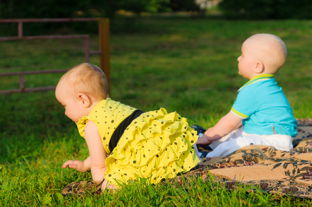 little girl in yellow dress and boy in blue shirt crawling on green grassの写真素材