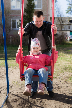 Father swinging daughter on a swing in the city.の写真素材