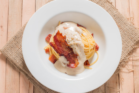 Bacon spaghetti in white plate on wooden background,from above.の写真素材