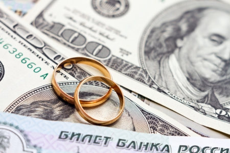 Wedding rings, gold chain and earrings in the form of hearts lie on moneyの写真素材