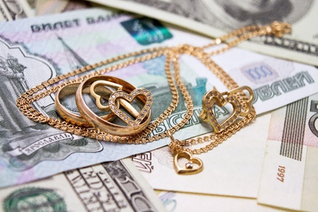 Wedding rings, gold chain and earrings in the form of hearts lie on moneyの写真素材
