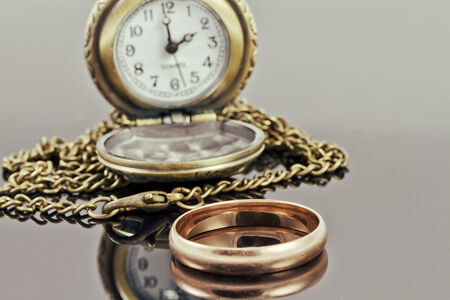 Pocket watch and a gold wedding ring on a reflective surfaceの写真素材