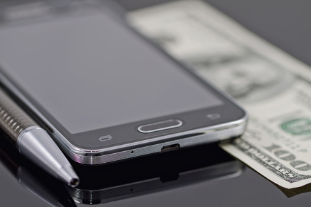 new smartphone, ballpoint pen and hundred dollars lying on a black reflective surfaceの写真素材