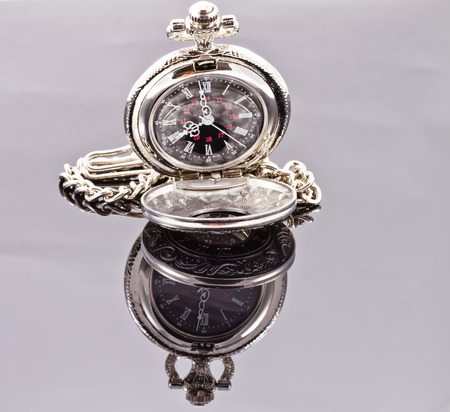 Silver pocket watch on a reflective surfaceの写真素材