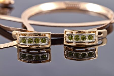 Beautiful and elegant gold earrings with emeralds against other gold jewelryの写真素材