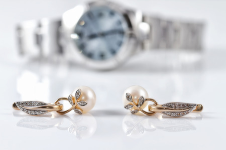 Gold earrings with pearl on the background of women's watchesの写真素材