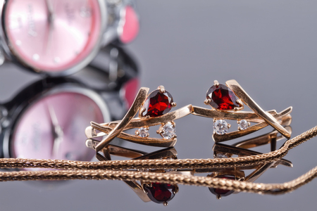 Gold earrings with rubies and gold chain on the background of elegant women's watchesの写真素材