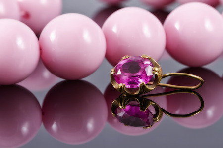 gold earring with ruby in the background of the necklace of large pink beadsの写真素材