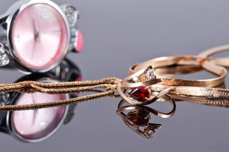Elegant Golden ring with a ruby and gold chain on the background of pink clocks.の写真素材