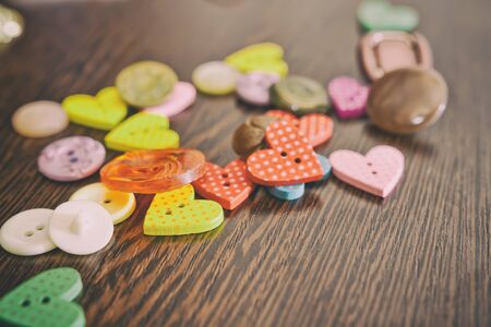 Buttons for garments of different shapes and colors lying on a wooden oak table