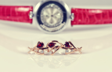 Gold earrings and rings with red rubies lie on the background of the unusual women's watches with red leather strapの写真素材