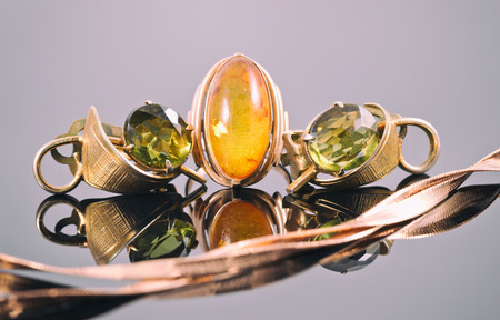Old gold earrings with green stones and a ring with amber in the background of a gold chainの写真素材