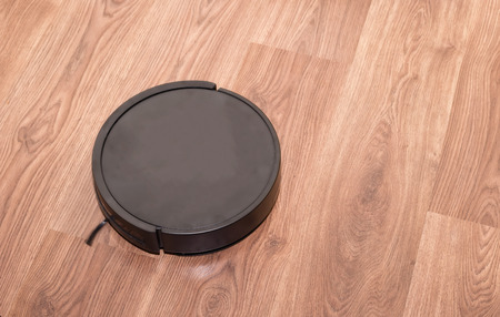 Small black vacuum robot is cleaning the apartment with wooden floorsの写真素材