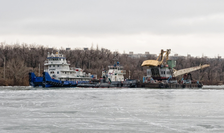 VOLGOGRAD, RUSSIA - NOVEMBER 27: River tug pusher drags a floating crane on a ship canal through the ice. November 27, 2016 in Volgograd, Russia.のeditorial素材