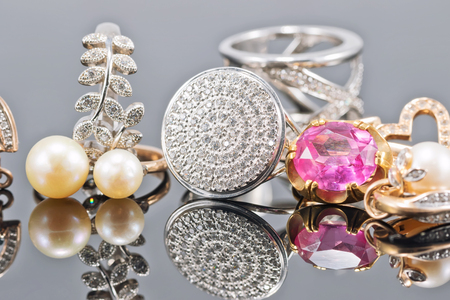 Gold and silver ornaments in different shapes and with different stones lie together on a reflective surfaceの写真素材