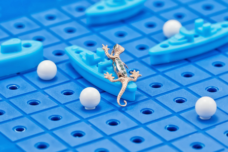 Pendant in the form of a gold Salamander attacks a toy warships on the playing field of Board gamesの写真素材