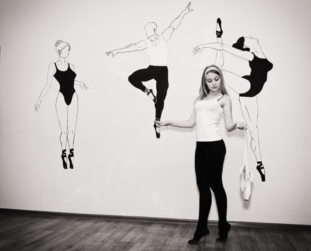Charming young dancer practicing in the hall and is standing on her toes in a ballet stance with Pointe shoes in hand. Black and white photoの写真素材