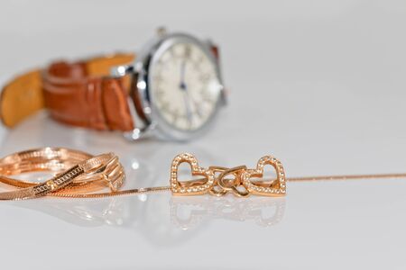 Gold earrings in the shape of a heart and chain with braided snake skin on a background of elegant women's watchesの写真素材