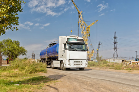 A truck with a tank for transportation of petroleum products traveling on a dusty road at an industrial areaの写真素材