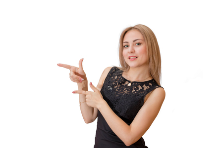 Smiling young blonde with a simple black dress points both hands to the left. Isolated portraitの写真素材