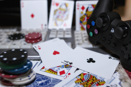 Desk of the player in online casinos with scattered cards and poker chips on the background of the keyboard and gamepadの写真素材