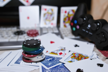 Desk of the player in online casinos with scattered cards and poker chips on the background of the keyboard and gamepadの写真素材