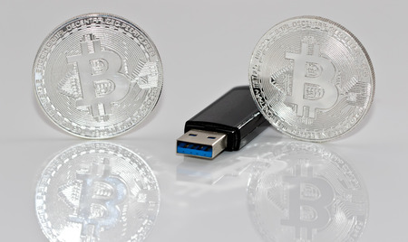 Souvenir silver coins bitcoin and USB flash drive with the information lie on the reflecting surfaceの写真素材