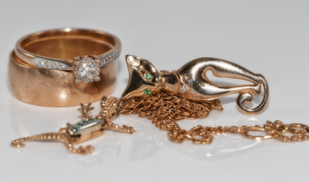 Gold rings, chains, earrings and pendants in the shape of salamanders and cat on a white reflective surfaceの写真素材