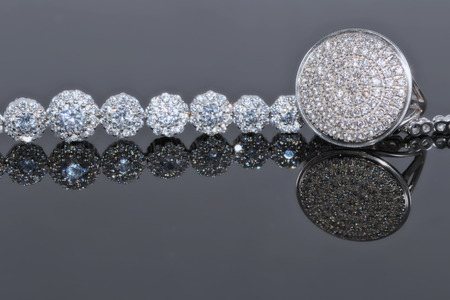 Silver bracelet with many sparkling diamonds and elegant ring with precious stones on a reflective surfaceの写真素材