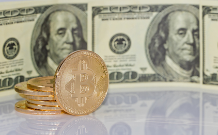 Gold souvenir coin bitcoin and a hundred-dollar bill lying on black reflective surfaceの写真素材