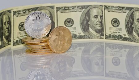 Gold souvenir coin bitcoin and a hundred-dollar bill lying on black reflective surfaceの写真素材