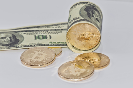Gold souvenir coin bitcoin and a hundred-dollar bill lying on reflective surfaceの写真素材