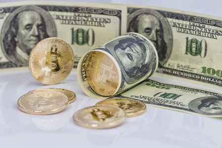 Gold souvenir coin bitcoin and a hundred-dollar bill lying on reflective surfaceの写真素材