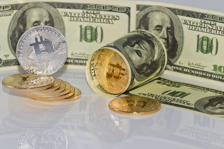 Gold souvenir coin bitcoin and a hundred-dollar bill lying on reflective surfaceの写真素材
