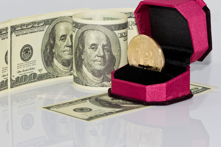 gold souvenir coin bitcoin lies in the gift box for jewelry on the background of dollarsの写真素材