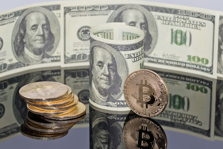 Gold souvenir coin bitcoin and a hundred-dollar bill lying on black reflective surfaceの写真素材