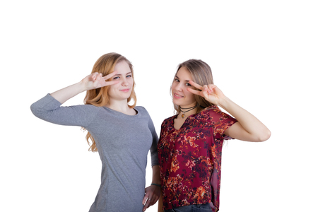 Two beautiful long-haired girls make a gesture of victory hands at the level of the face. Isolated on white backgroundの写真素材