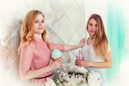 Two cute girls with long hair in dresses drink drinks from cups with lids and tubesの写真素材