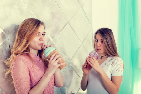 Two cute girls with long hair in dresses drink drinks from cups with lids and tubesの写真素材