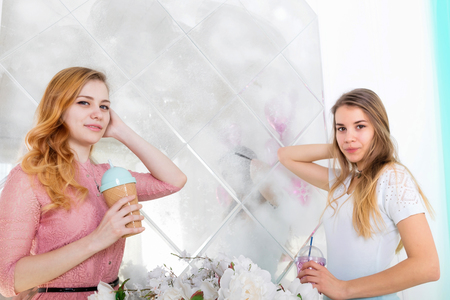Two cute girls with long hair in dresses drink drinks from cups with lids and tubesの写真素材