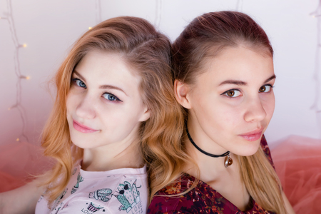Close-up portrait of two pretty girls sitting in a pose back to backの写真素材