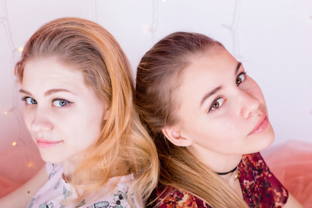 Close-up portrait of two pretty girls sitting in a pose back to backの写真素材