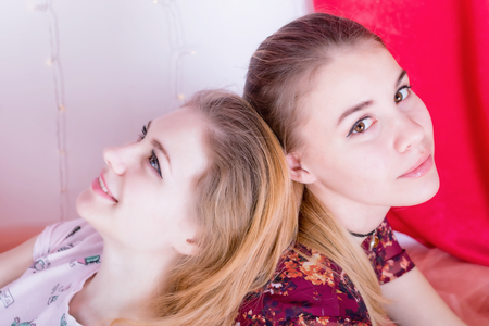 Close-up portrait of two pretty girls sitting in a pose back to backの写真素材