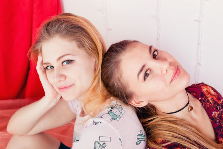 Close-up portrait of two pretty girls sitting in a pose back to backの写真素材