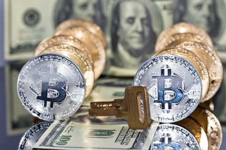 A stack of bitcoin gold coins and the key to the monetary vault lie against the background of hundred dollar banknotes on the reflective surfaceの写真素材