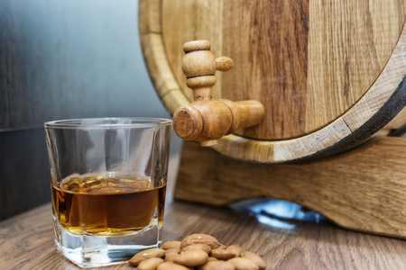 A small wooden oak barrel for home production of beer, cognac and whiskey and a glass of whiskey aged in itの写真素材