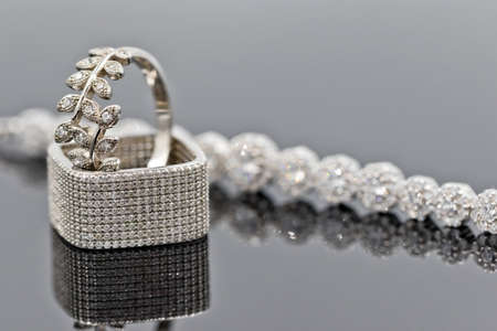 Elegant square silver ring with cubic Zirconia with other silver ornaments on reflective surfaceの写真素材