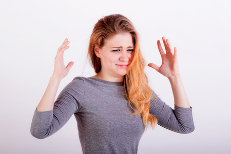 Portrait of a very upset young woman with long red hair and blue eyes with raised hands