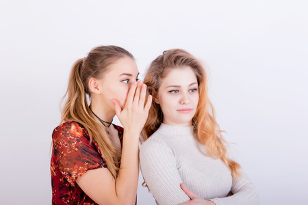 Two beautiful young girls share gossip every whisper in ear